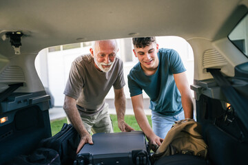 Wall Mural - Two men Teenager and senior grandfather pack baggage in trunk of car