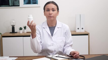 Poster - Virtual Prescription: During an online call with a patient, a female doctor holds a bottle of pills or vitamins on her desk, conducting telehealth consulting and prescribing medication. 