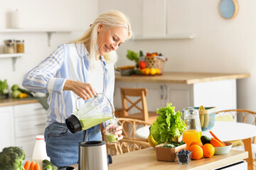 Canvas Print - Mature woman pouring healthy smoothie into glass in kitchen