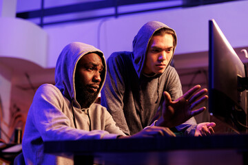 Poster - Criminals hacking server together and discussing password cracking malware. Confused african american and asian hackers in hoods checking malicious software on code on computer screen