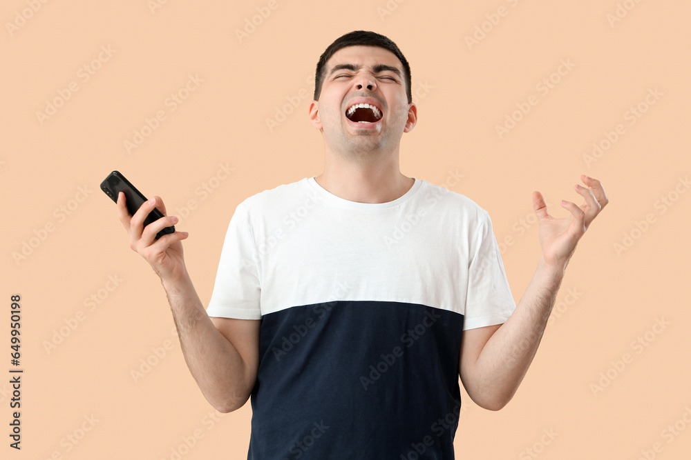 Stressed young man with smartphone on beige background