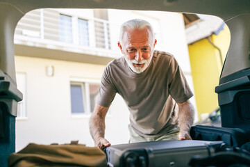 Wall Mural - One senior man travel concept male put suitcase in trunk of the car