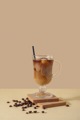 Wall Mural - Glass of ice coffee with straw and beans on yellow table near beige wall