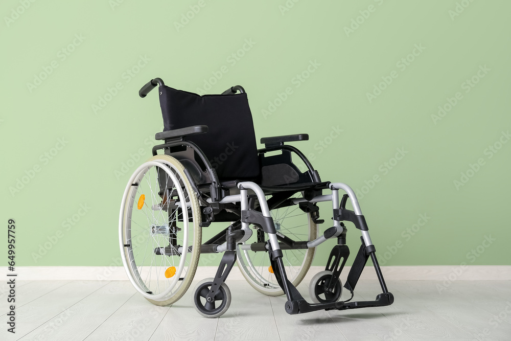 Modern empty wheelchair near green wall