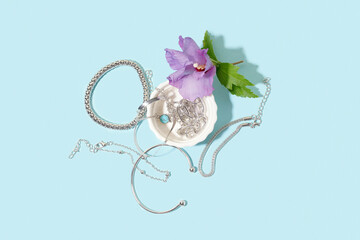 Wall Mural - Bowl with different beautiful silver bracelets and flower on blue background