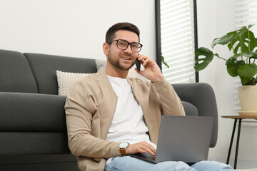 Wall Mural - Man talking on smartphone while working with laptop at home