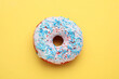 Glazed donut decorated with sprinkles on yellow background, top view. Tasty confectionery