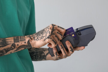 Wall Mural - Tattooed young man paying with credit card via terminal on light background, closeup