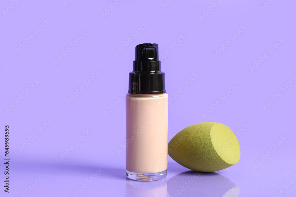 Bottle of makeup foundation and sponge on purple background