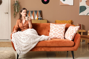 Poster - Young woman with cup of tea and plaid resting at home on autumn day