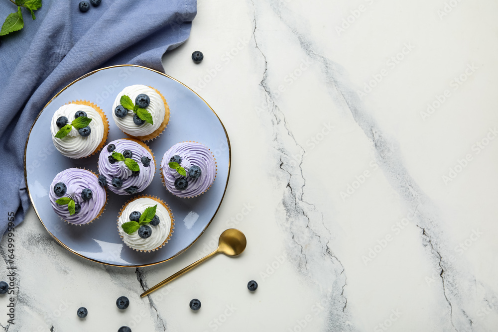 Plate of delicious cupcakes with blueberries and mint on white background