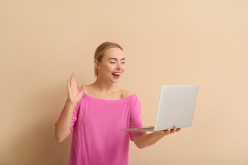 Wall Mural - Happy young woman with laptop waving hand on beige background