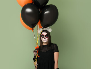 Wall Mural - Young woman dressed for Halloween with balloons on green background