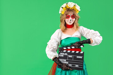 Poster - Young woman with painted skull on her face and clapperboard against green background. Halloween celebration