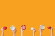 © Pixel-Shot - Hands holding different alarm clocks and cups on yellow background