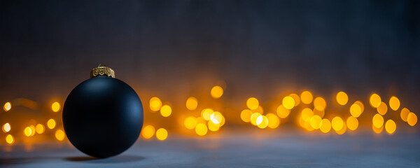 Wall Mural - dark christmas background with one black bauble and warm cozy bokeh in the background. christmas and