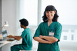 © DragonImages - Portrait of smiling medical nurse in green scrubs crossing arms and looking at camera