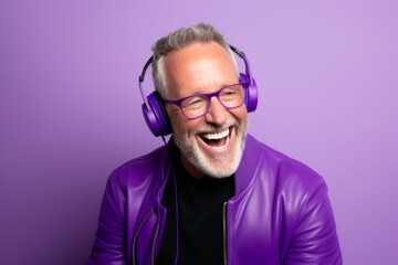 Portrait of a happy senior man listening to music with headphones on purple background