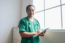 Young Asian Male Doctor Smiling While Holding Medical Records At Hospital