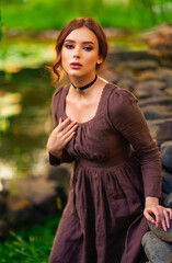 Wall Mural - Beautiful red haired girl in brown long medieval dress and black vintage choker sitting on stone wall. Art work of romantic lady.Pretty tenderness model posing on nature.