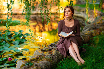 Wall Mural - Beautiful red haired girl in brown long medieval dress and black vintage choker sitting on stone wall. Art work of romantic lady with book.Pretty tenderness model posing on nature.