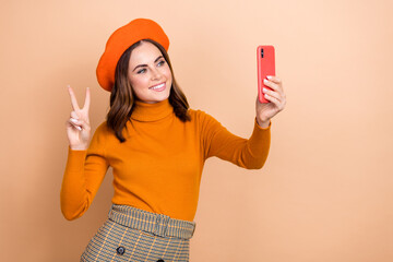 Canvas Print - Photo of charming blogger wear autumn orange outfit make self picture look camera recording video v-sign isolated on beige color background