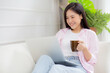© NT_studio - Young asian business woman work from home with laptop computer and drinking coffee on sofa in living room, freelance girl using notebook sitting on couch with comfort and relax, lifestyles concept.