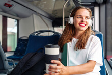 Brunette Woman Wearing Red Lipstick, White Tee Shirt Sits In City Shuttle Bus And Listening To Music Using Her Headphones.