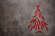 Chili pepper in the shape of a Christmas tree on a brown dark background. Abstract Christmas tree made of chili pods and red peppercorns. Top view, flat lay.