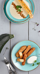 Wall Mural - An assortment of delectable zucchini dishes beautifully presented on ceramic plates. From creamy zucchini soup to crispy tempura, set against a gray wooden backdrop with utensils