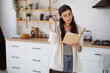 © Dmytro Hai - Brunette woman holding pencil while reading book in kitchen at home, personal growth concept