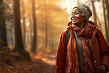 A Senior African American Woman Is Is Walking On A Forest Trail Enjoying The Surroundings With An Autumn Coat In A Calm And Tranquil Forest During Sunset - Relaxing Walking Activity In Spare Time Or B