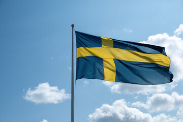 Canvas Print - Sweden national flag waving on a flagpole, blue cloudy sky background