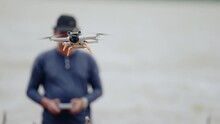 Man controls the drone using sticks on the remote control landing drone in his hands after recording video and flying in natural scenic place.