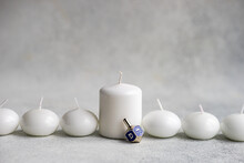 Ivory Colored Scented Candles With Blue Hanukkah Dreidel Placed On Concrete Background
