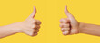 Two female hands showing thumbs up sign against yellow background
