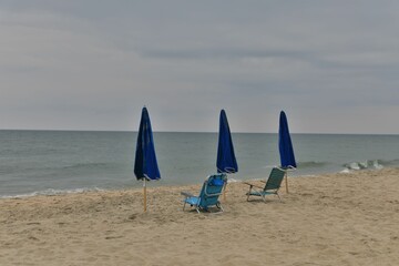 Canvas Print - some chairs on the beach with blue umbrellas by the water