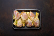 Raw uncooked chicken legs in green marinade with seasonings in black plastic container top view on dark rustic background. Preparing healthy meal with marinated chicken drumsticks.