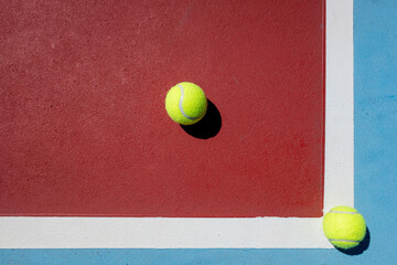 Top view of two tennis balls on a red and blue court