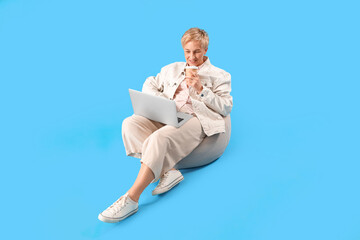 Sticker - Mature female programmer with laptop and cup of coffee sitting on blue background