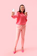 © Pixel-Shot - Young woman in stylish suit with cup of coffee taking selfie on pink background