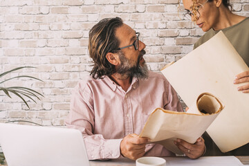 Couple of adult business colleagues working together at the desk with laptop and big paper design. People and office home workplace lifestyle. Small business concept job indoor. Online smart working