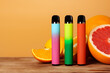Three electronic cigarettes with citrus fruits on orange background