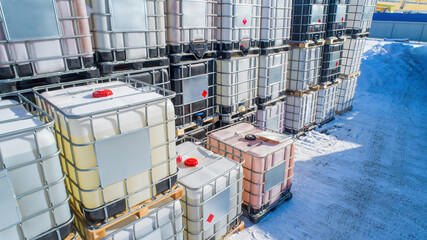 Poster - Plastic reservoirs on pallets. Tanks for transportation liquids. Plastic barrels for oil products. Warehouse with containers in open air. Reservoirs in metal crate on snow. Reservoirs for chemicals