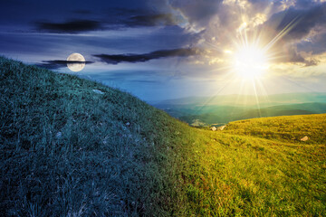 Wall Mural - green grass on hillside meadow in high mountains under the cloudy blue sky with sun and moon at twil