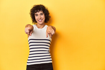 Caucasian curly-haired woman in white tank-top cheerful smiles pointing to front.