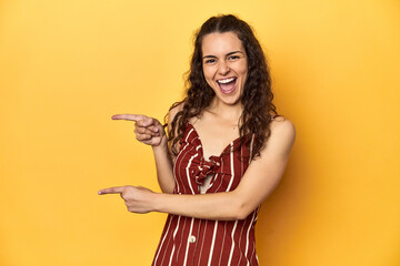 Canvas Print - Young Caucasian woman, yellow studio background, pointing with forefingers to a copy space, expressing excitement and desire.