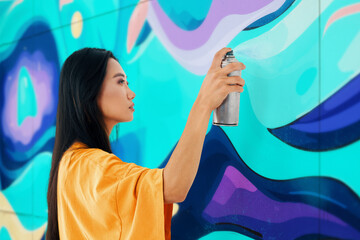 Female street artist painting colorful graffiti on wall