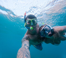 Wall Mural - Beautiful and cute couple of millennials young people snorkeling and diving together looking underwater for fishes and coral having fun and enjoying. Summer time swimming in the sea blue ocean.
