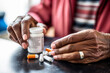 © OpticalDesign - African american old man taking pills, mature hands taking medication out of prescription bottle close up, painkillers and health care concept, black